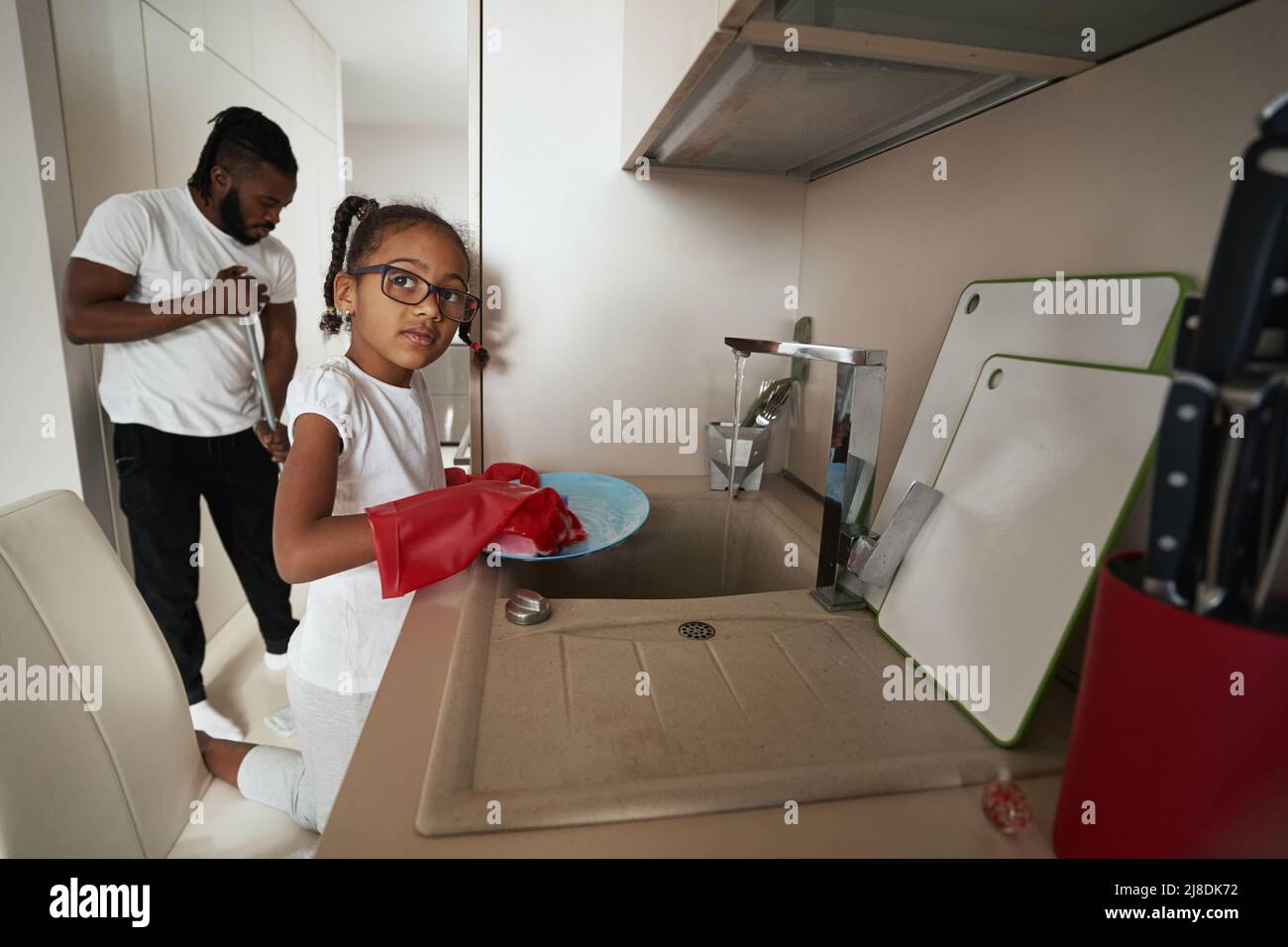 Little girl washes dishes in kitchen next to adult man Stock Photo Alamy