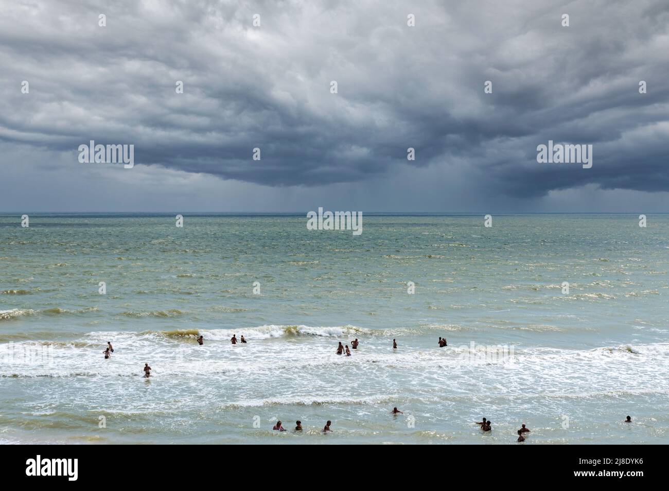 Sea beach before the storm. Thunderclouds are approaching the beach, rain in the distance. People want to swim in the sea despite the danger. Stock Photo