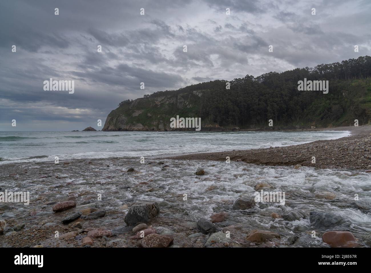 A river flows into the ocean at a rocky beach in a small picturesque ...