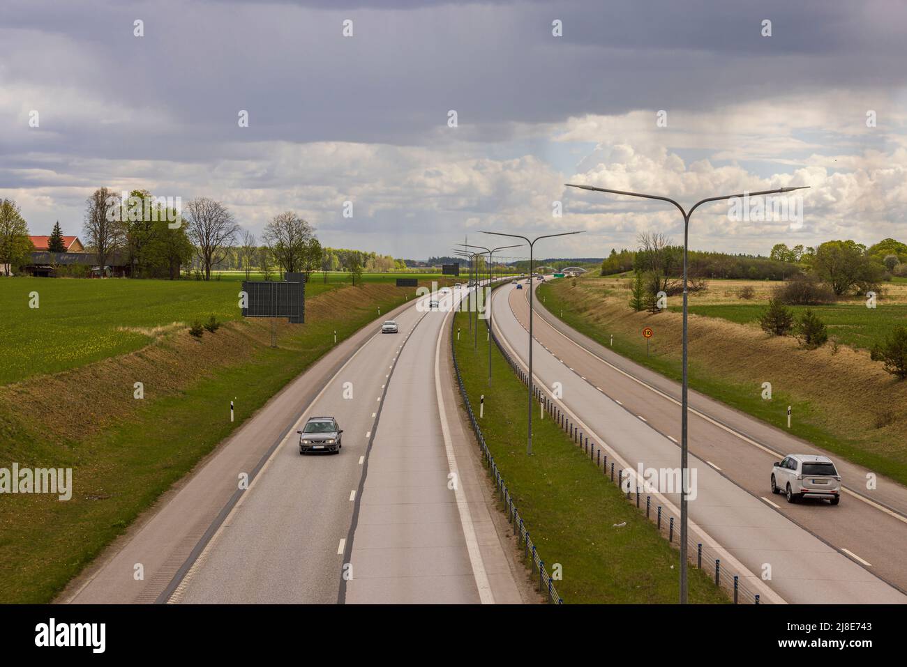 Beautiful top view of E4 highway with several cars. Green side fields and stormy sky background. Sweden. Stock Photo