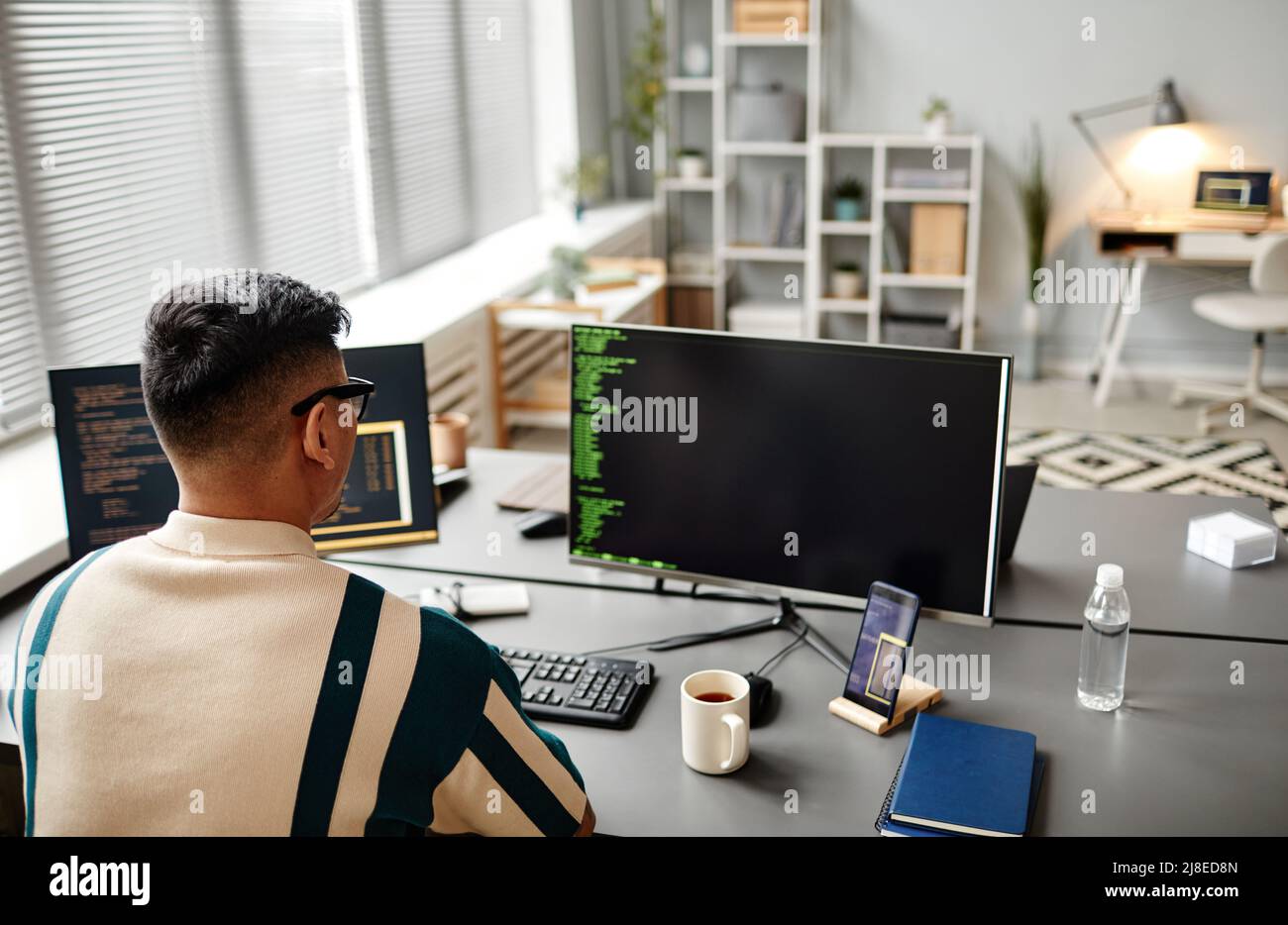Back view of male IT developer typing on keyboard with programming code ...