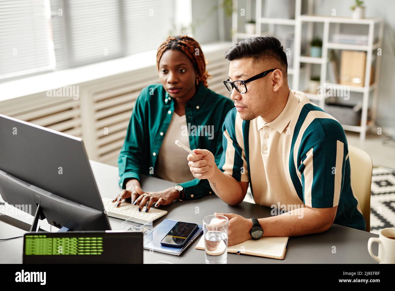 Portrait of diverse software development team using laptop while working at desk in office setting Stock Photo