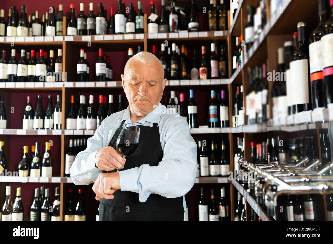 senior man professional sommelier tasting red wines in wine store Stock Photo