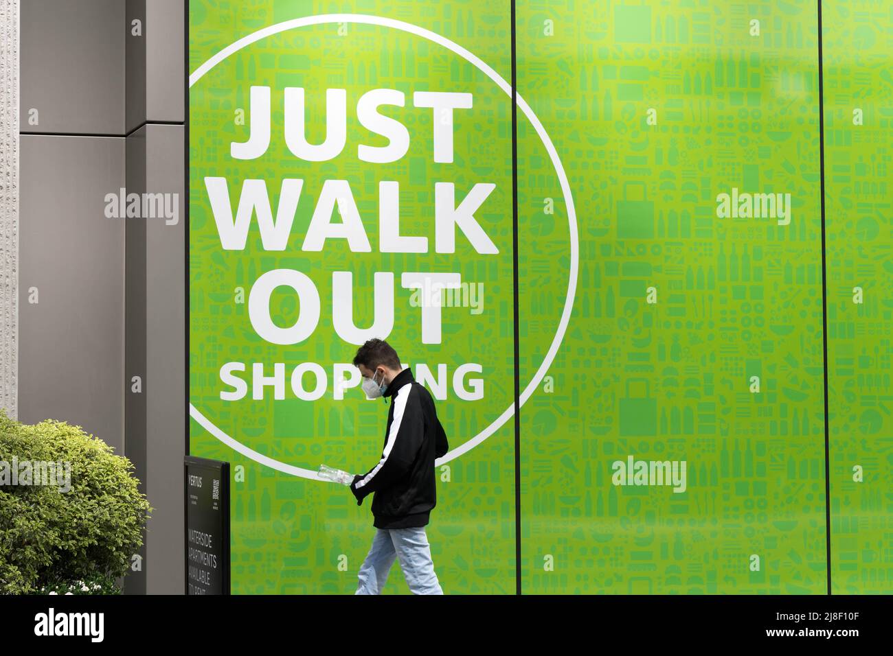 man in face mask shopper outside the amazon grocery shop 'amazon just walk out shopping sign' London England UK Stock Photo