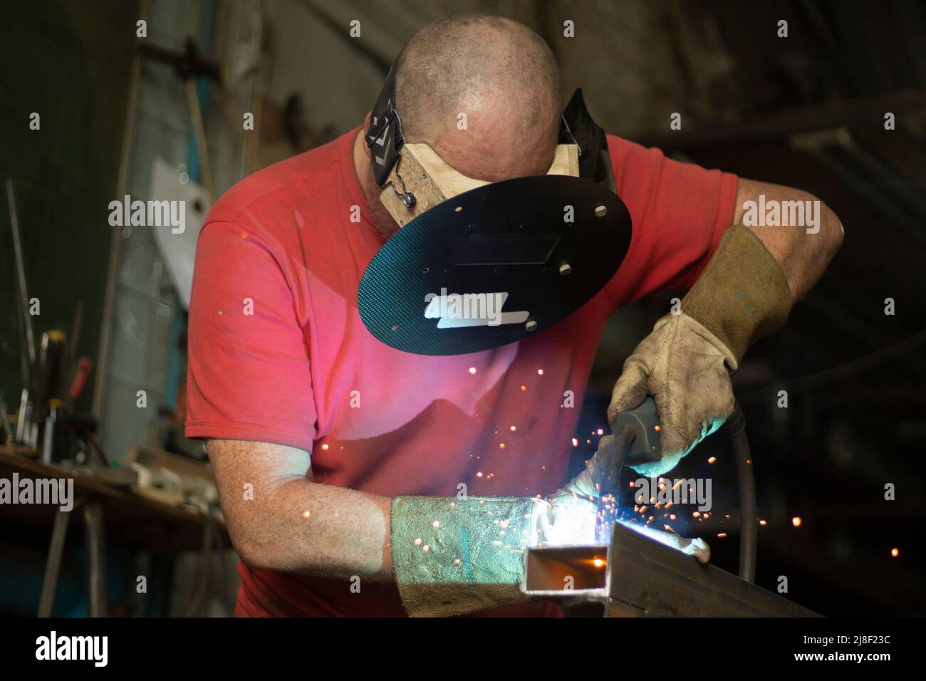 A masked welder works in a workshop. The man works with metal. The guy works in the workshop. Welding of steel seam. Stock Photo