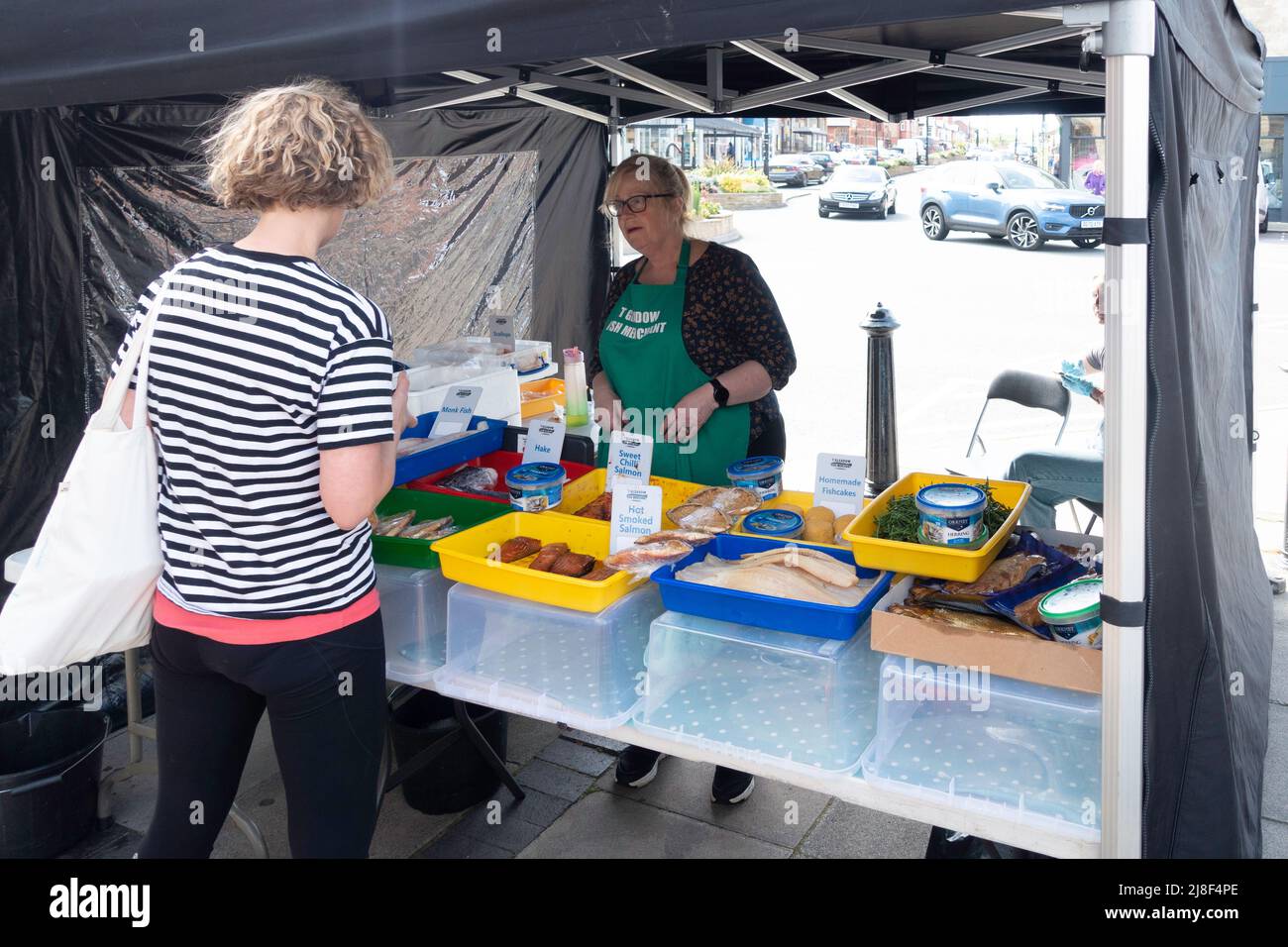 A blond lady customer with Fishmonger lady stallholder with display of her fresh fish for sale in Saltburn Farmers Market in Spring  2022 Stock Photo