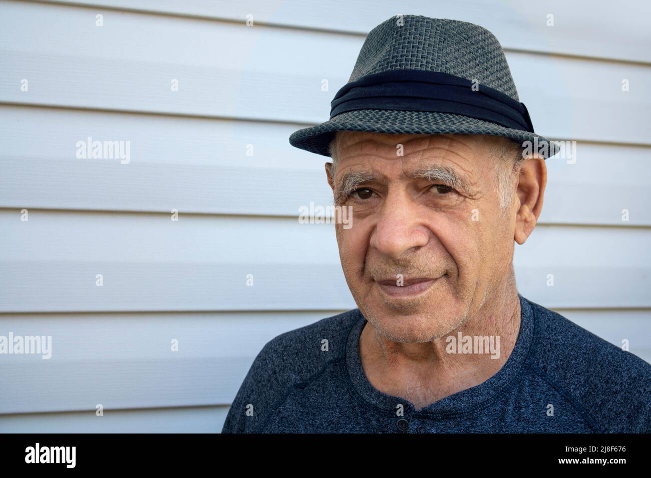 caucasian male senior adult with a fedora hat in front of an exterior white house wall Stock Photo