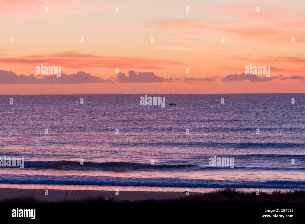 A single isolated open fishing boat sits off the shoreline in pre dawn light and calm weather at Culburra Beach, New South Wales, Australia Stock Photo