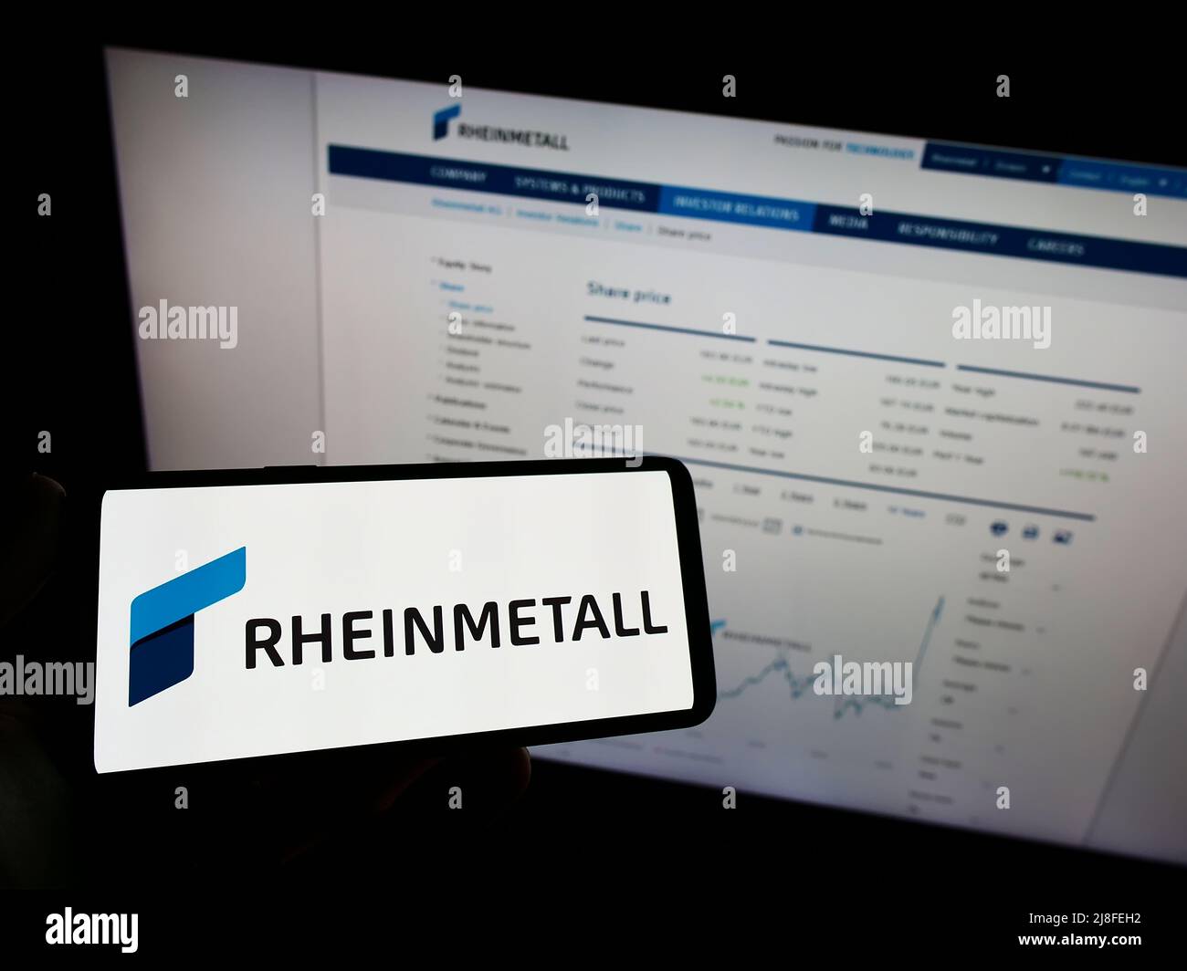 Person holding mobile phone with logo of German defence company Rheinmetall AG on screen in front of business web page. Focus on phone display. Stock Photo