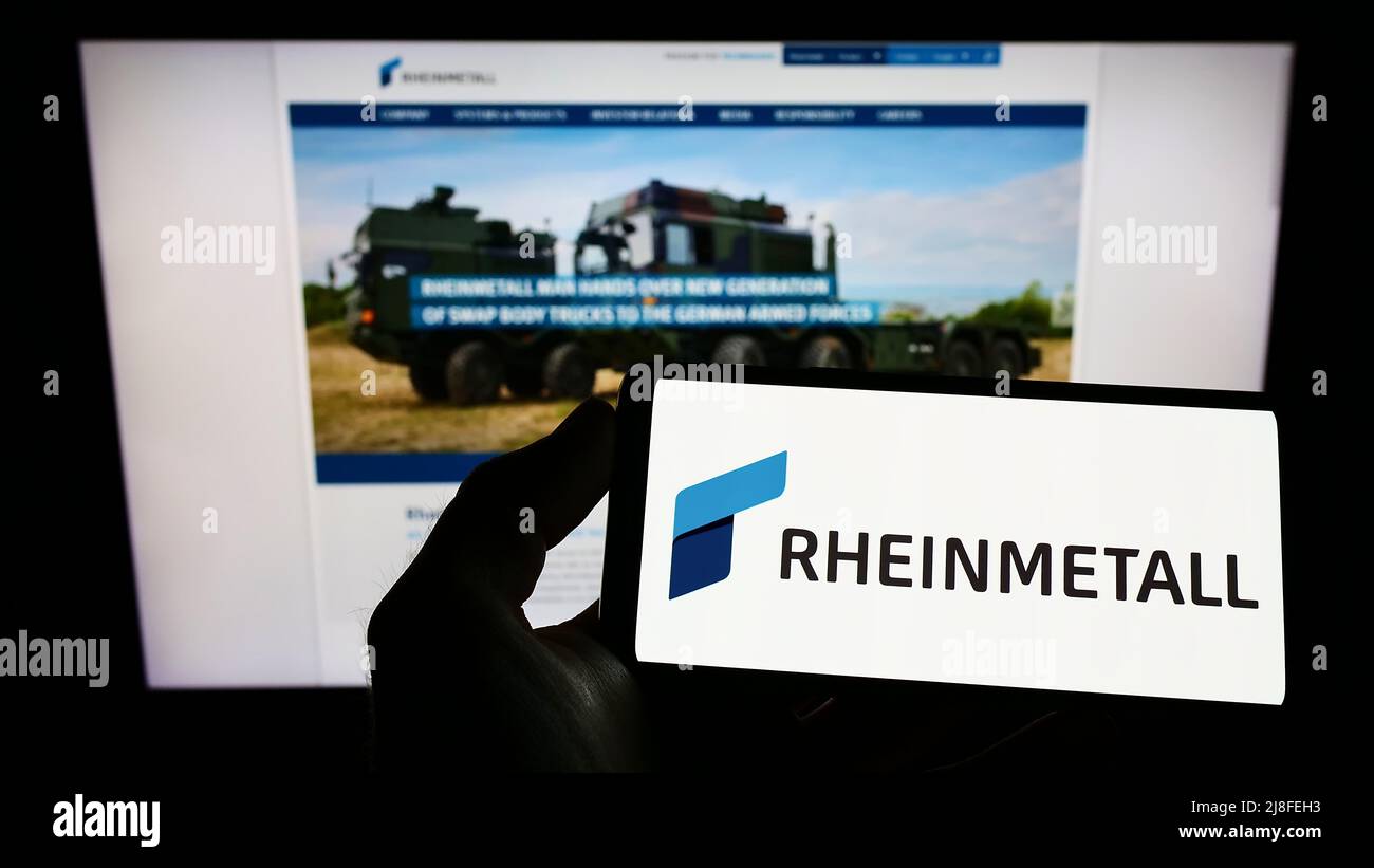 Person holding smartphone with logo of German defence company Rheinmetall AG on screen in front of website. Focus on phone display. Stock Photo