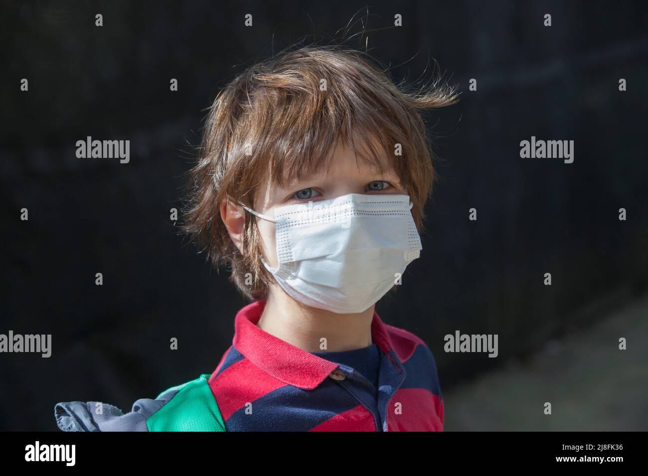 6 years little boy wearing a face mask straight into the camera. He has a stiff gesture Stock Photo