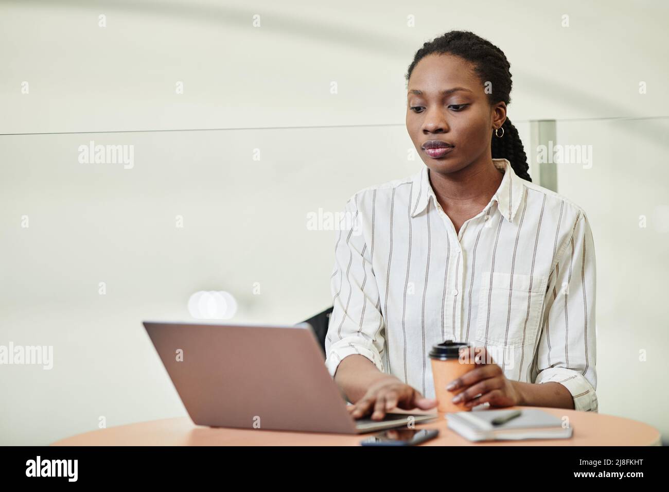 Minimal portrait of young black woman using laptop while working in ...