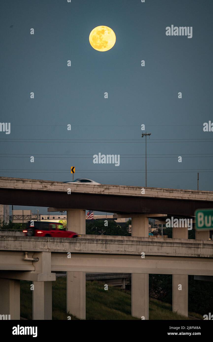 Austin, Texas, USA. 15 May, 2022. The full moon rises over the city of Austin, 183 North overpass is seen in the foreground.  This first sign of red is from the sunset, but the moon on Sunday night, May 15th is called the Super Flower Blood Moon. Later this evening there will be an eclipse which will give the moon a red colour. It is called the Flower moon because of the abundance of flowers growing in May. Credit: Sidney Bruere/Alamy Live News Stock Photo