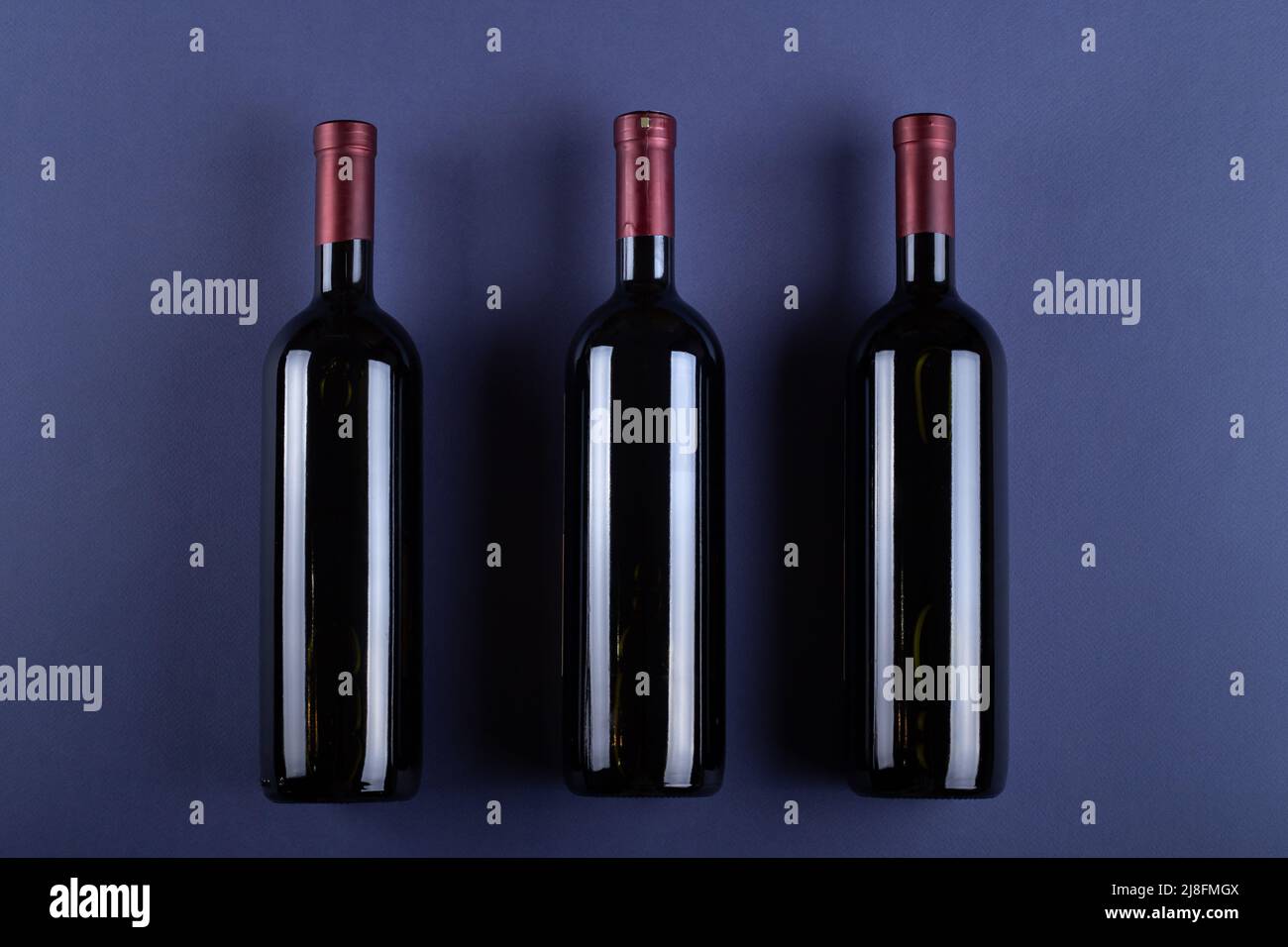 Three bottle of red wine without a label on a purple paper background