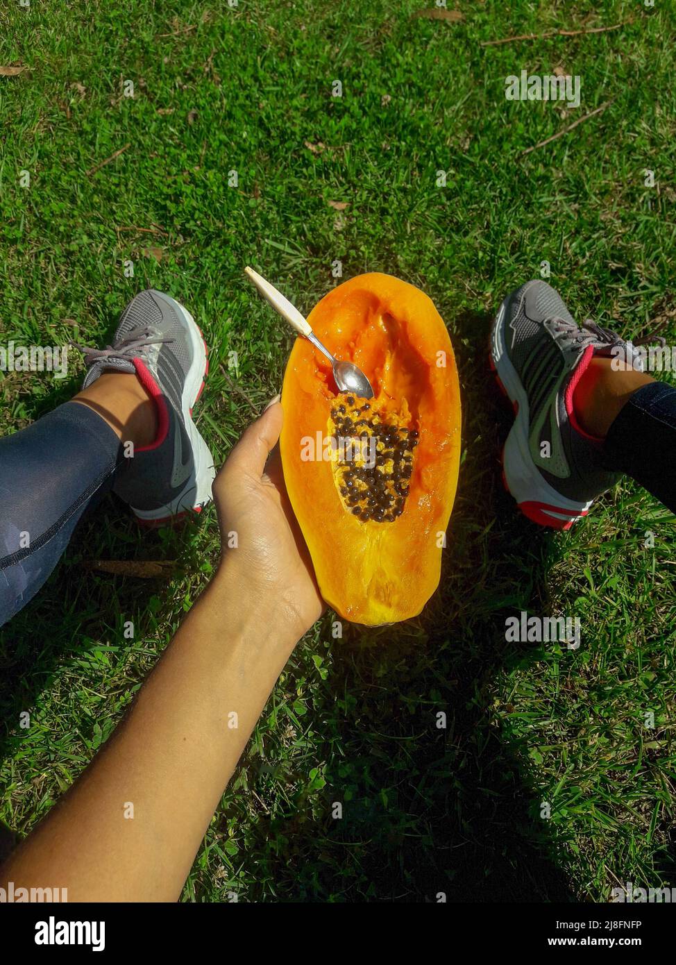 girl sits on a lawn and holds a half of delicious papaya with a spoon Stock Photo