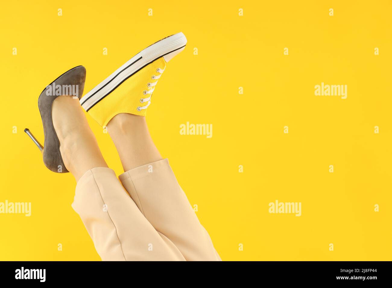 Female legs in heel and sneaker on yellow background Stock Photo