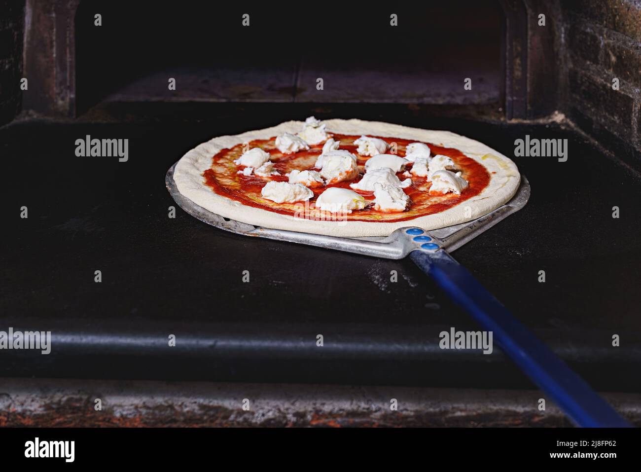 The pizza maker inserts a traditional margherita pizza with mozzarella and tomato morsels in the