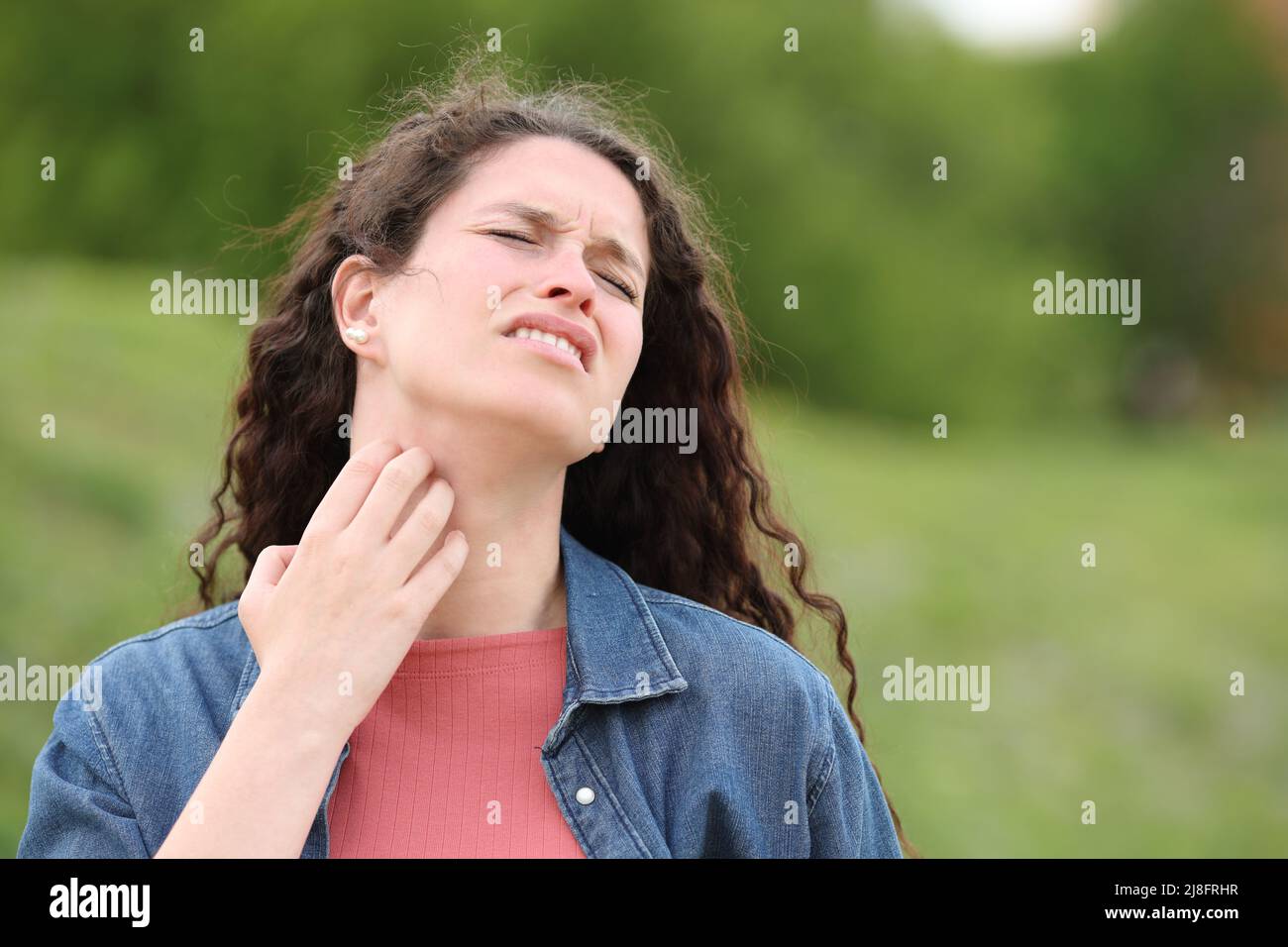 Overwhelmed woman scratching itchy neck standing in a park Stock Photo
