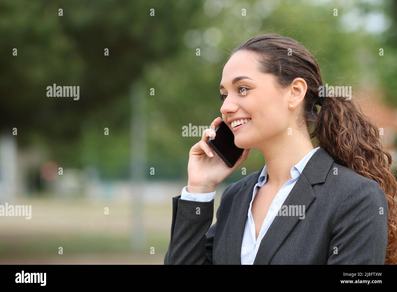 Happy businesswoman talking on cell phone walking in a park Stock Photo