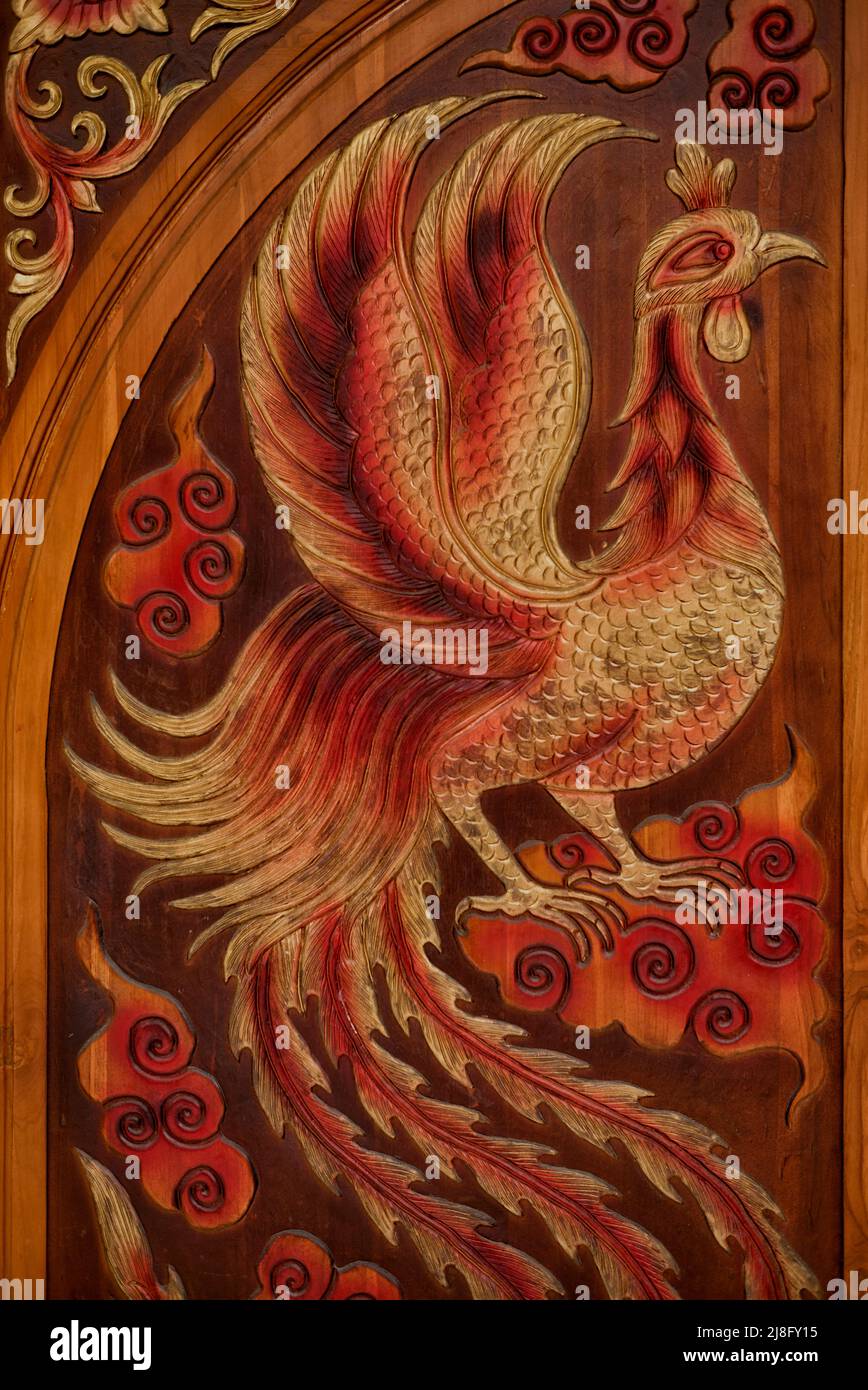Carved wood door detail featuring rooster chicken figures with impressive plumage Thailand Southeast Asia Stock Photo