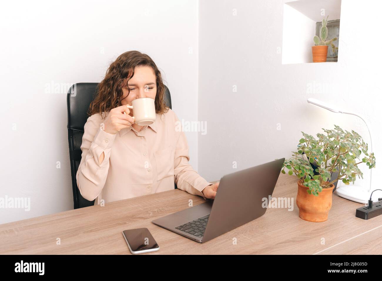 Photo of young woman worker sitting at desk and drinking her morning coffee, more energy. Stock Photo