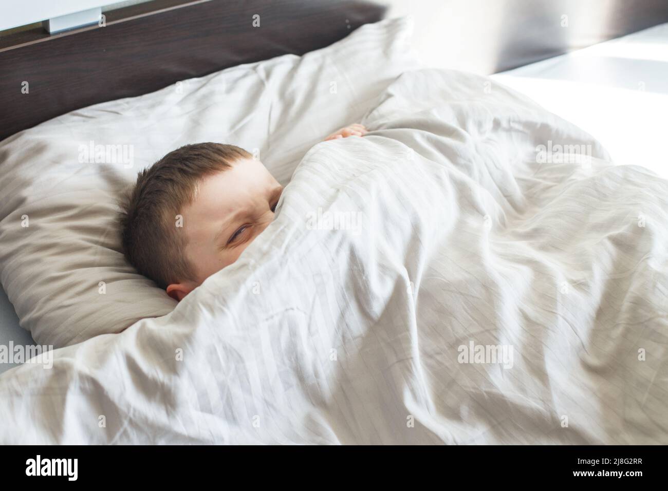 boy sleep in the bed. the child lies on a pillow and covers his face with a blanket Stock Photo Alamy