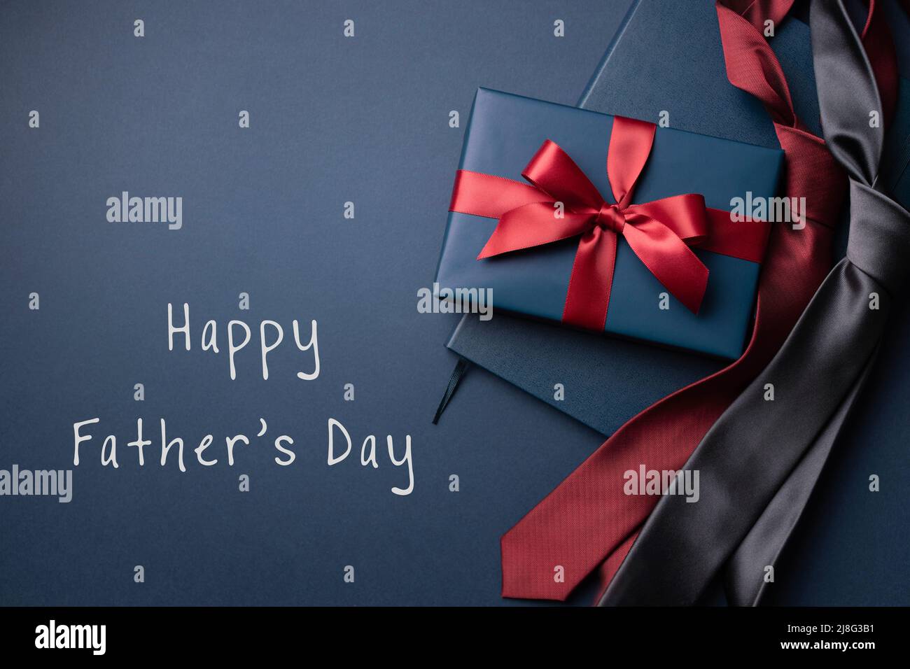 Happy Father's Day card with blue gift box, notebook and neckties on dark blue background. Stock Photo