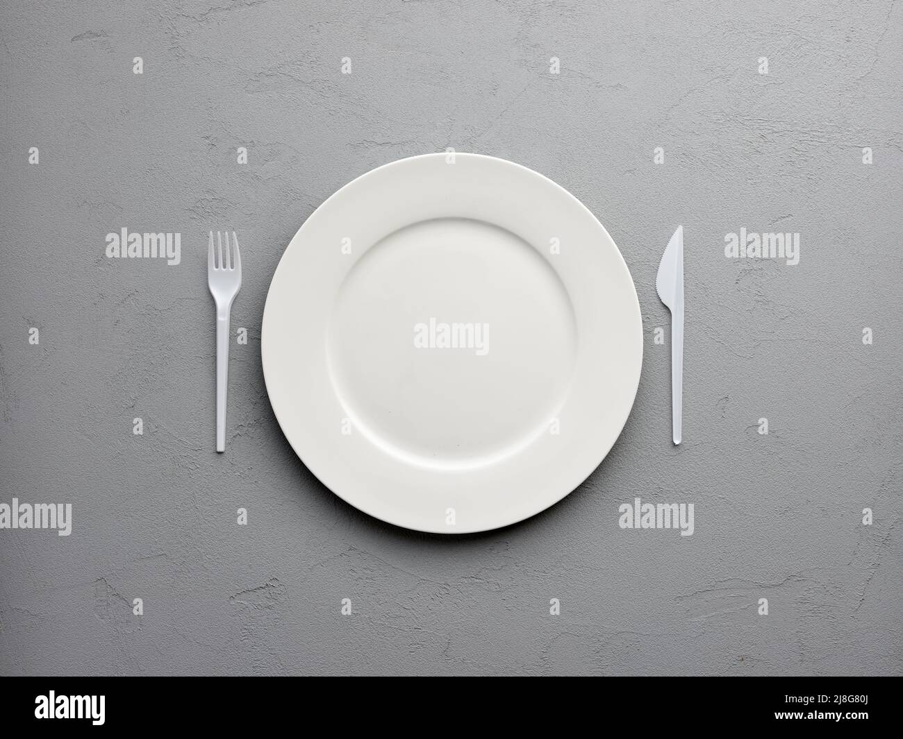 White round empty plate with fork and knife on textured gray background. Stock Photo