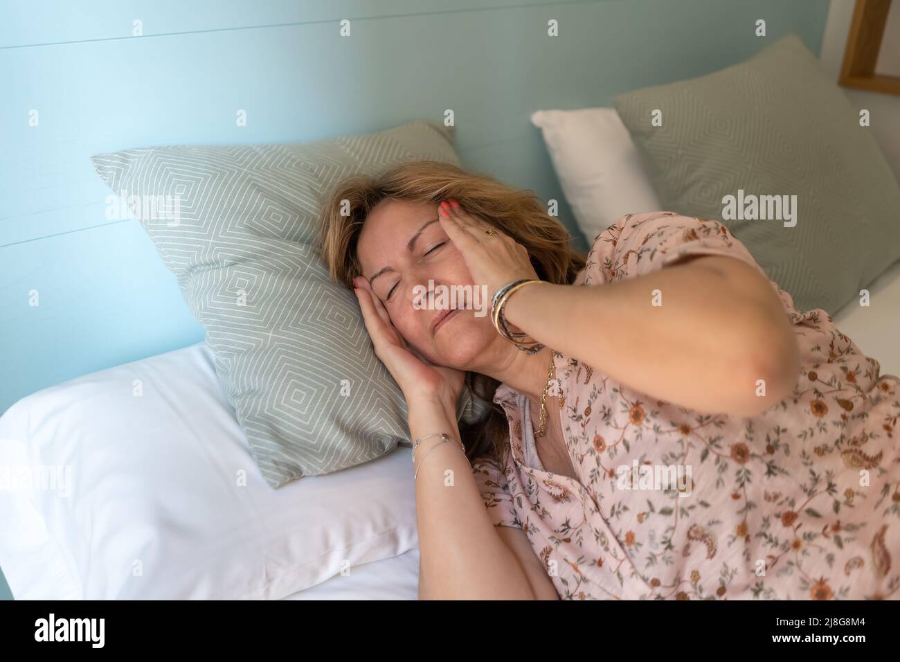 Senior woman with severe headache lying on the bed in her room Stock