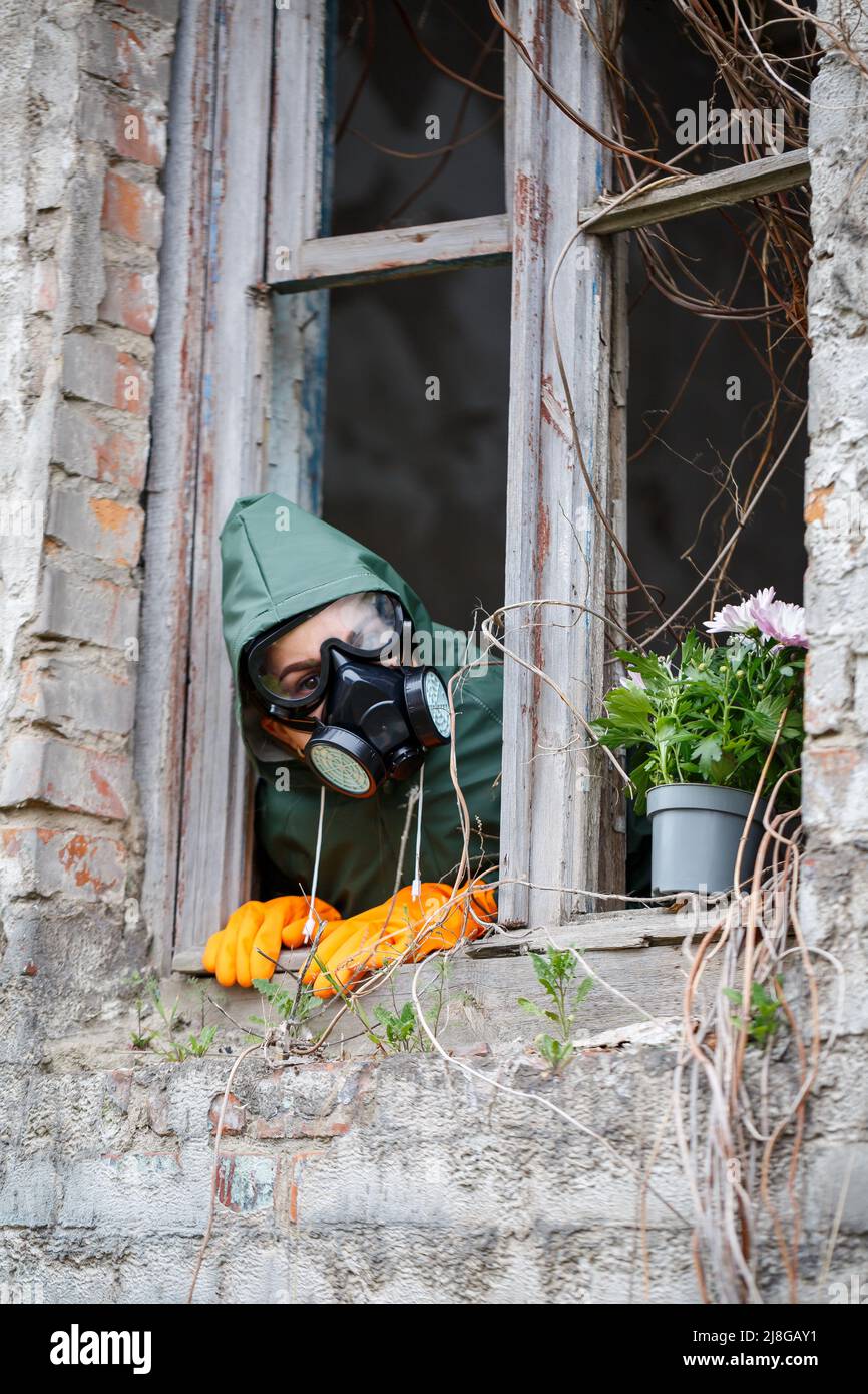 A man in a raincoat and gas mask collects a flower from a scorched, poisonous earth. Air pollution concept. Ecological catastrophy. Stock Photo