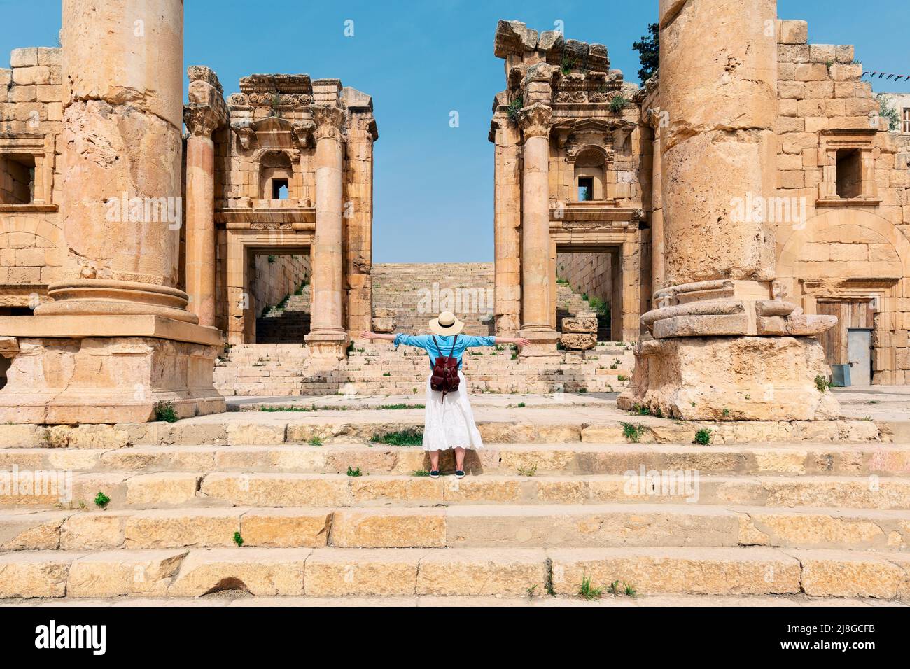 Young tourist standing with hat and open arms  in old city of Jerash, ancient building in Jordan. Hellenistic ruins of Qasr al-Abd Stock Photo
