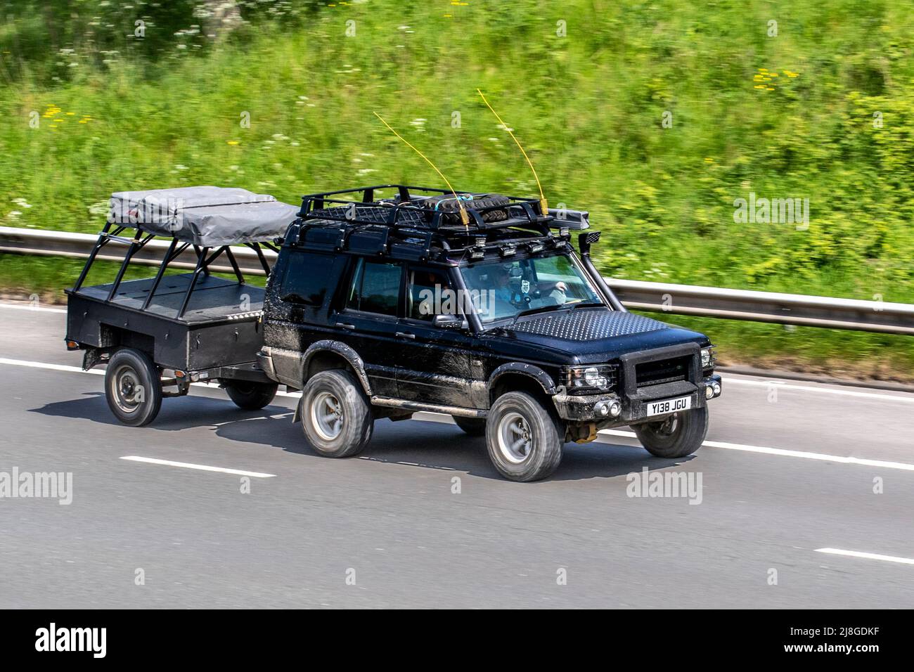 Dirty, Mud spattered 2001 black custom Expedition Land Rover Discovery 2495cc towing camping trailer; driving on the M61 Motorway, Manchester, UK Stock Photo