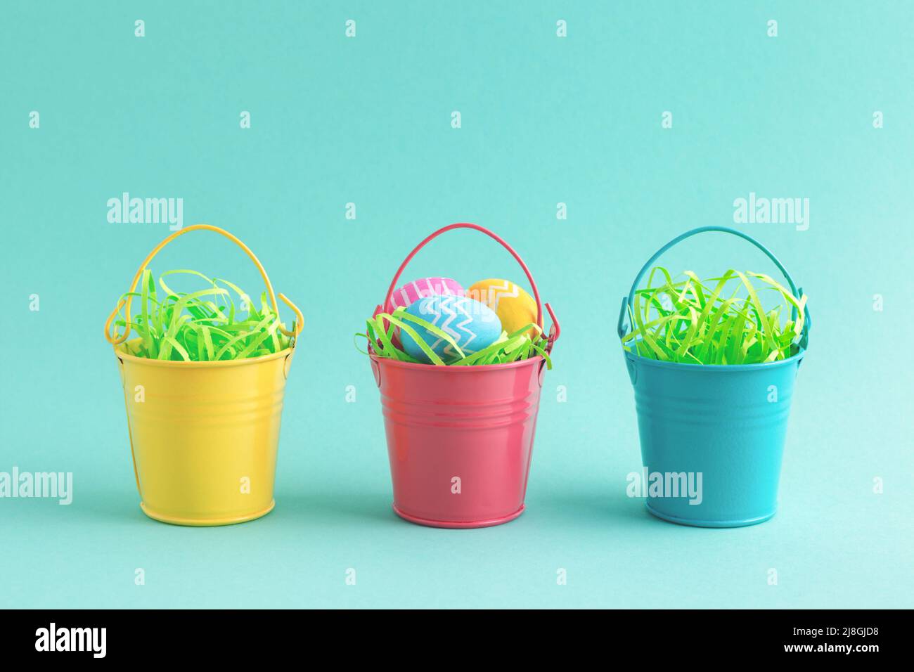Easter holiday card with row of colourful eggs in yellow, blue and red decorative buckets isolated on pastel turquoise background. Egg hunt concept. Stock Photo