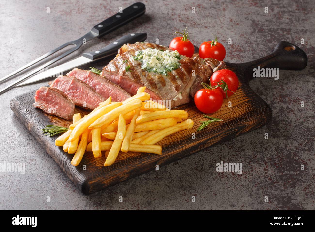 Grilled Ribeye Steak with French Fries, green butter and tomatoes closeup on the wooden board on the table. Horizontal Stock Photo