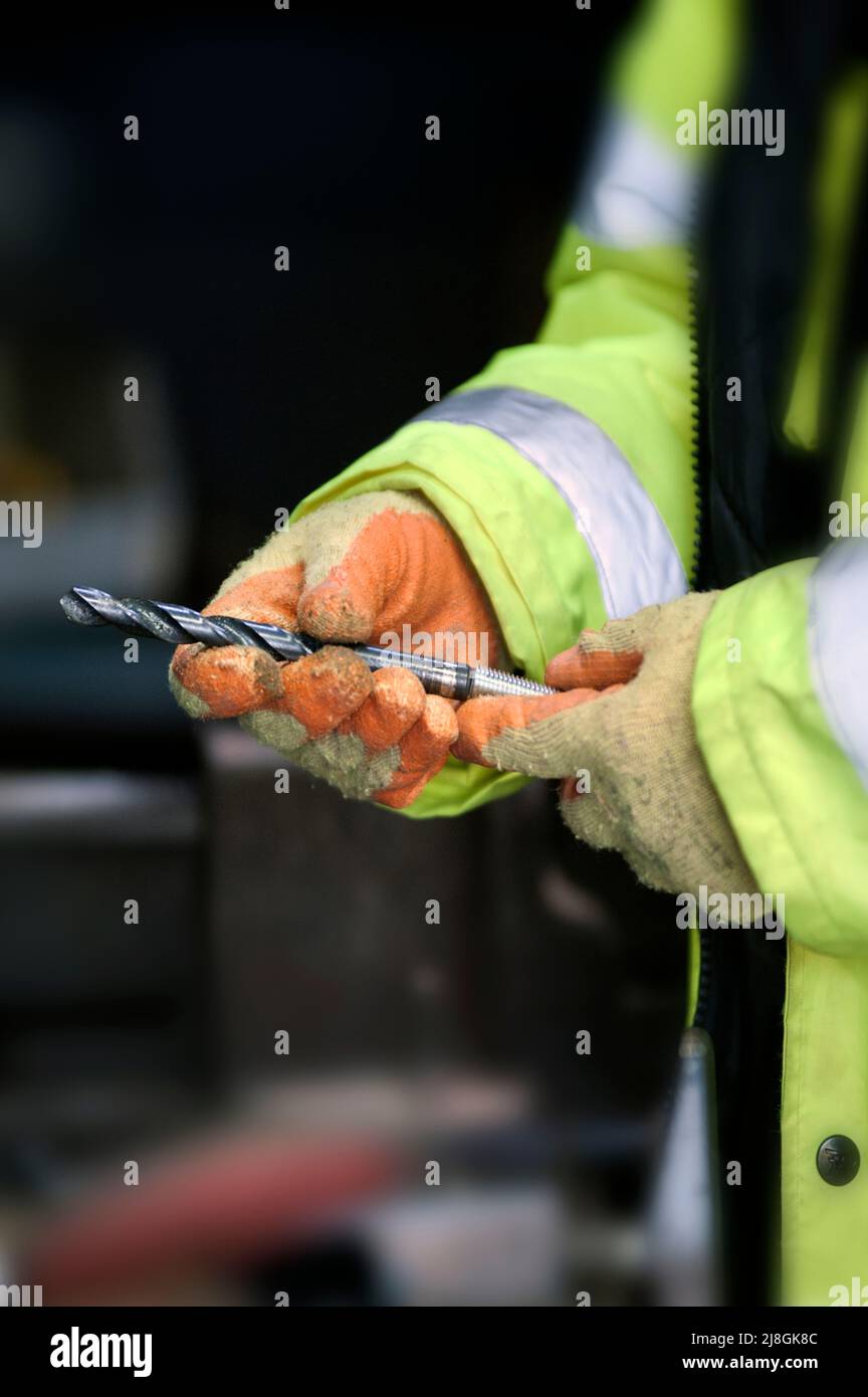 gloved hands holding metal twist drill bit Stock Photo