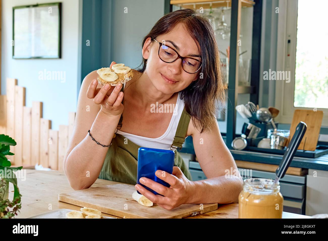 Woman enjoying her healthy breakfast checking on her smart phone at home. Brunch with puffed corn cakes, peanut butter and banana. Protein diet concep Stock Photo