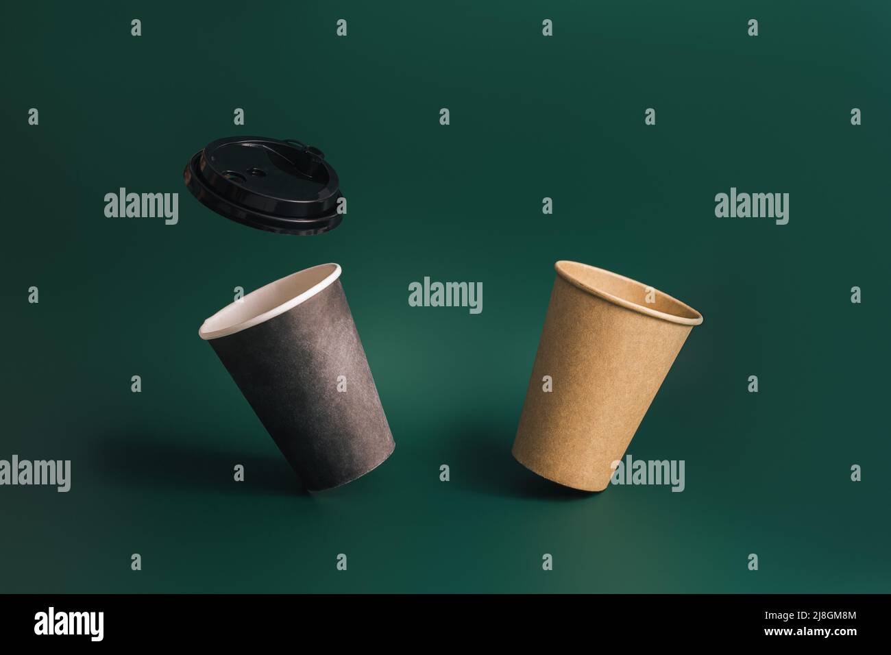 Two floating disposable cups and lid against green background Stock Photo
