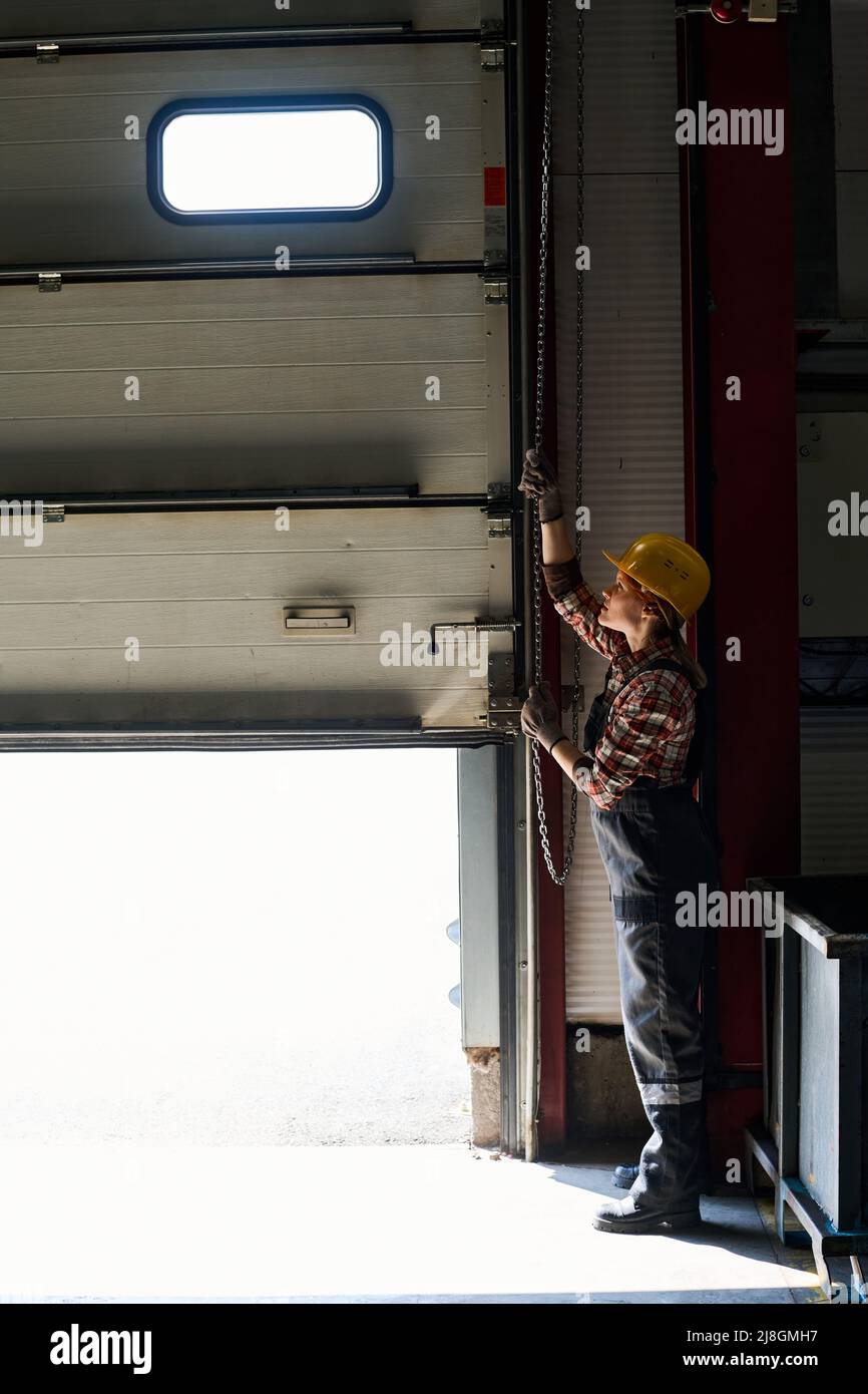 Young female engineer opening shutter roller door of garage, hangar or
