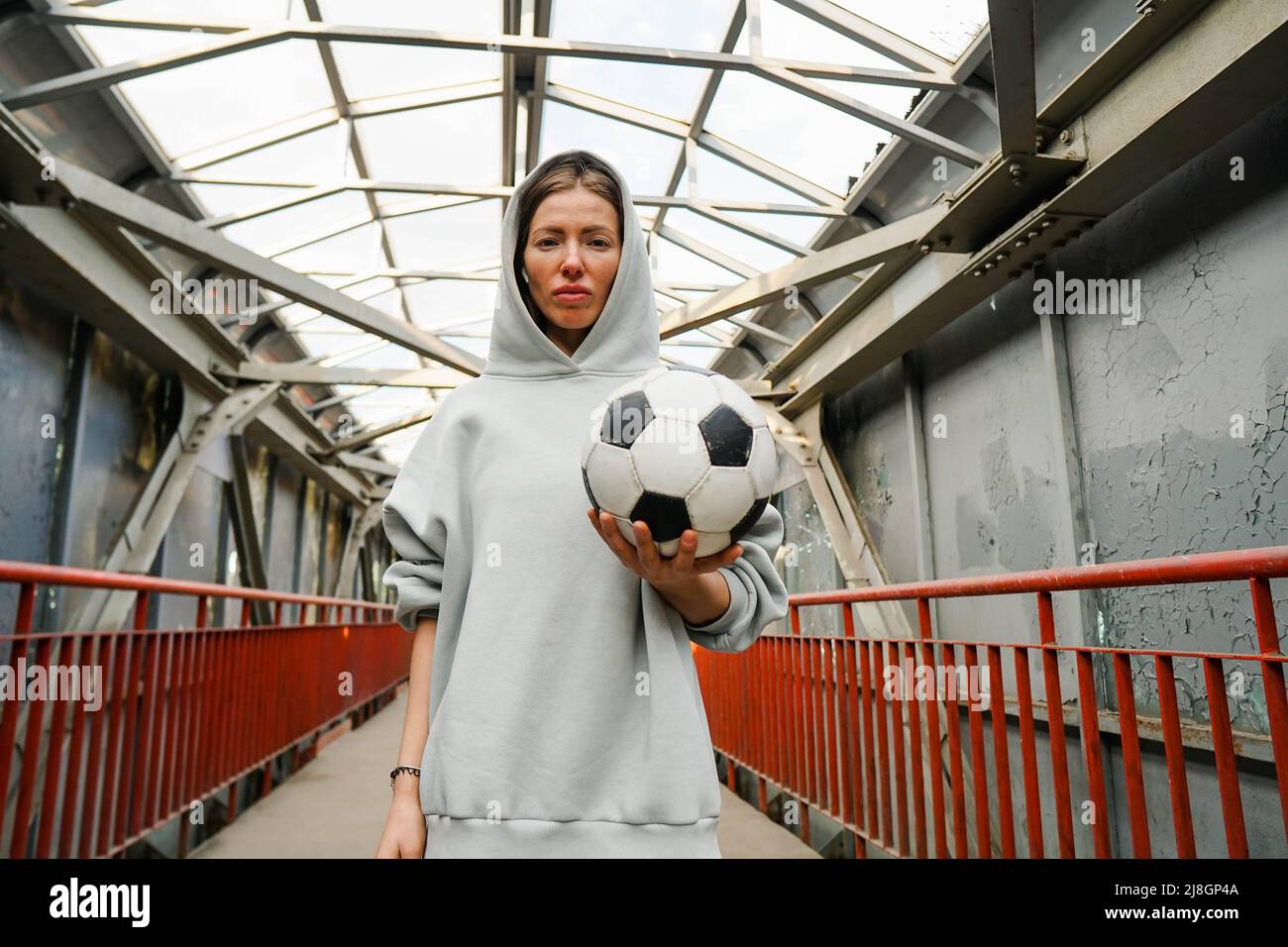Young sporty woman football player wearing hoodie hold soccer ball on