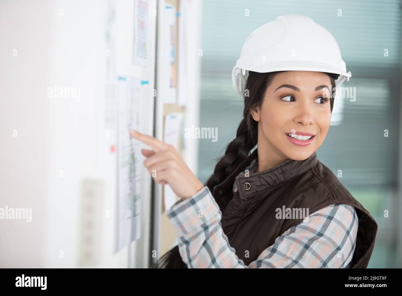 woman wearing a safety helmet pointing to notice board Stock Photo Alamy