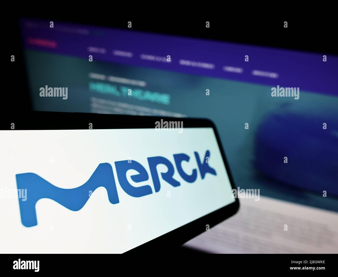 Cellphone with logo of German chemicals company Merck KGaA on screen in front of business website. Focus on center-left of phone display. Stock Photo