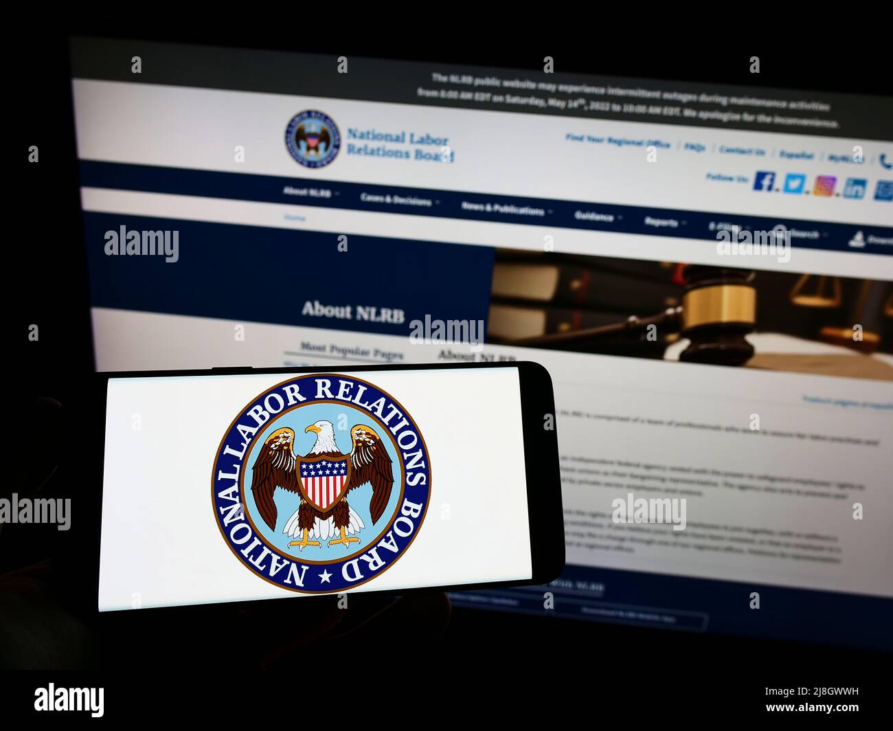 Person holding mobile phone with logo of American National Labor Relations Board (NLRB) on screen in front of web page. Focus on phone display. Stock Photo