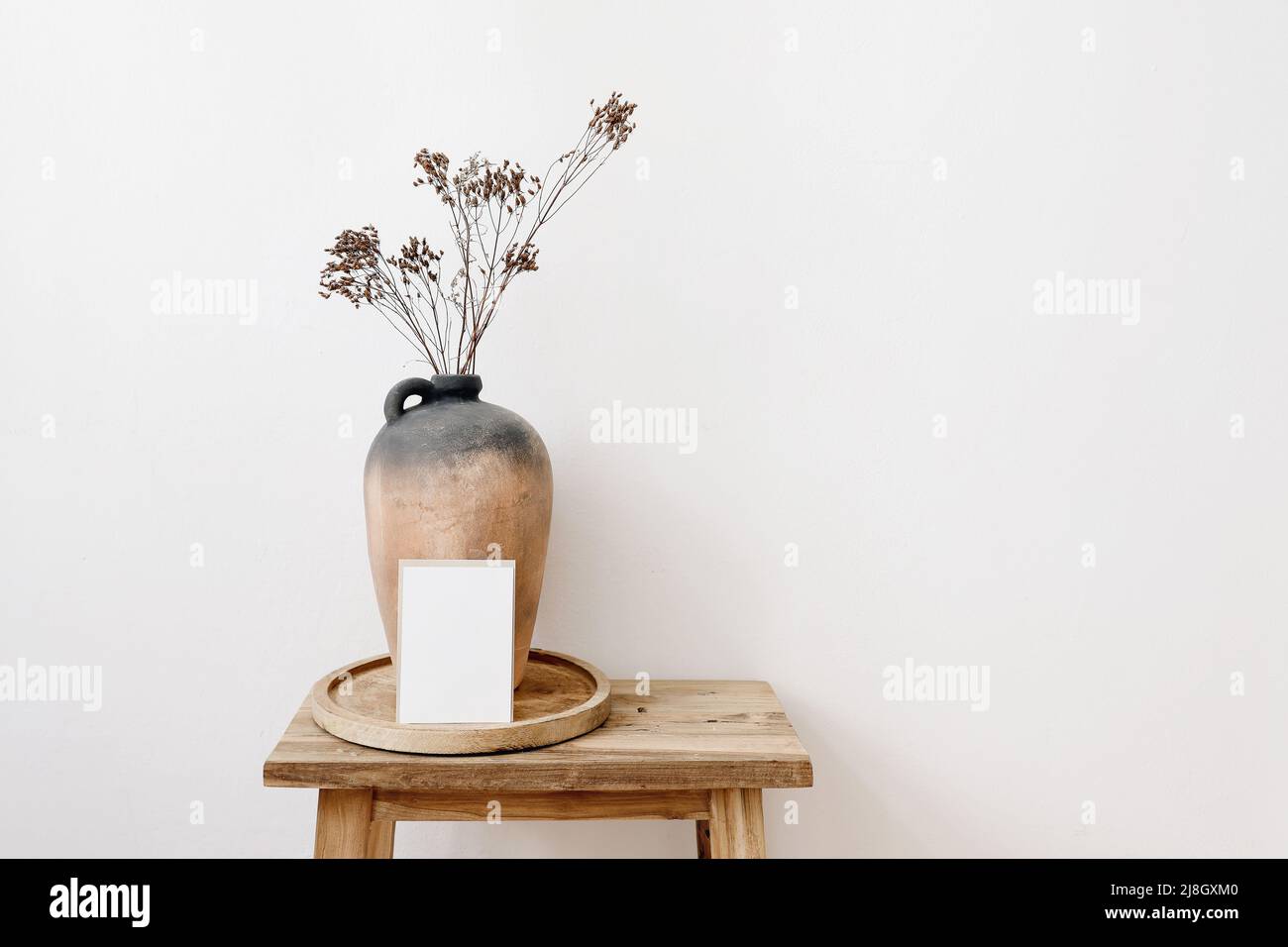 Elegant minimal stationery mockup. Blank greeting card, invitation. Rustic clay vase, pitcher with dry grass, hypericum flowers on old wooden stool Stock Photo