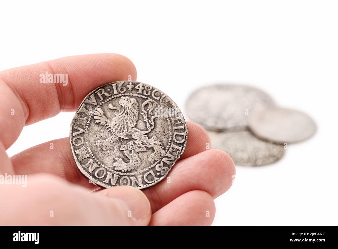 Male hand holding old silver thaler with lion on reverse. Old coins on white background. Lion Daalder. Selective focus Stock Photo