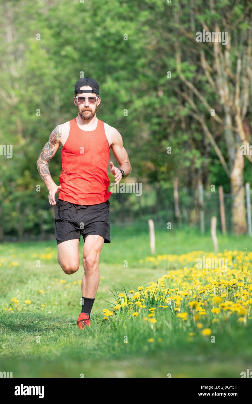 A male athlete with a tattoo on his right arm during a trail training run in the spring meadow Stock Photo