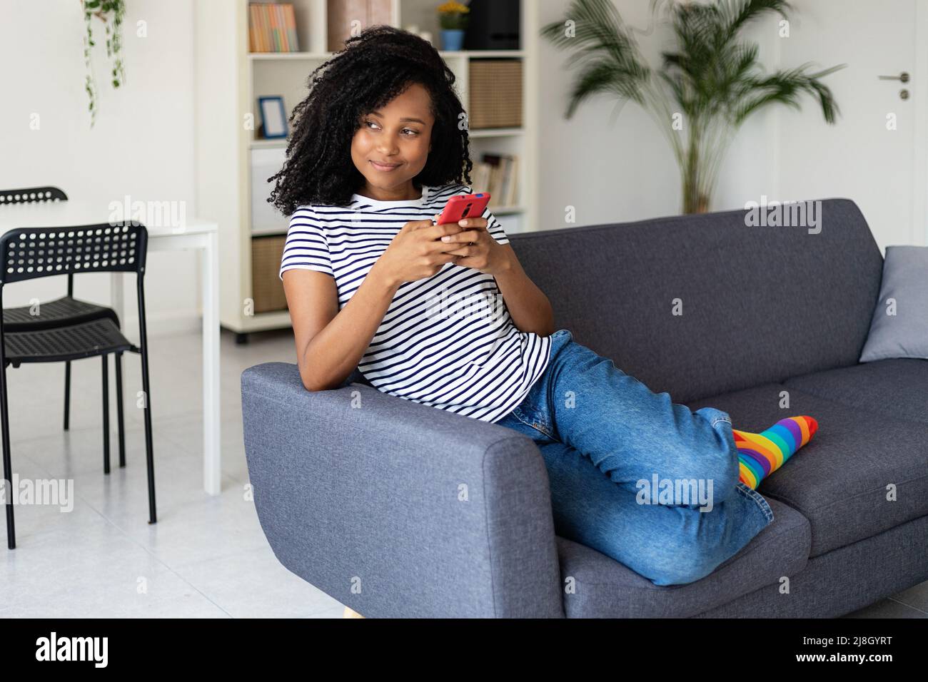 Smiling african american woman using mobile phone relaxing on sofa at home Stock Photo
