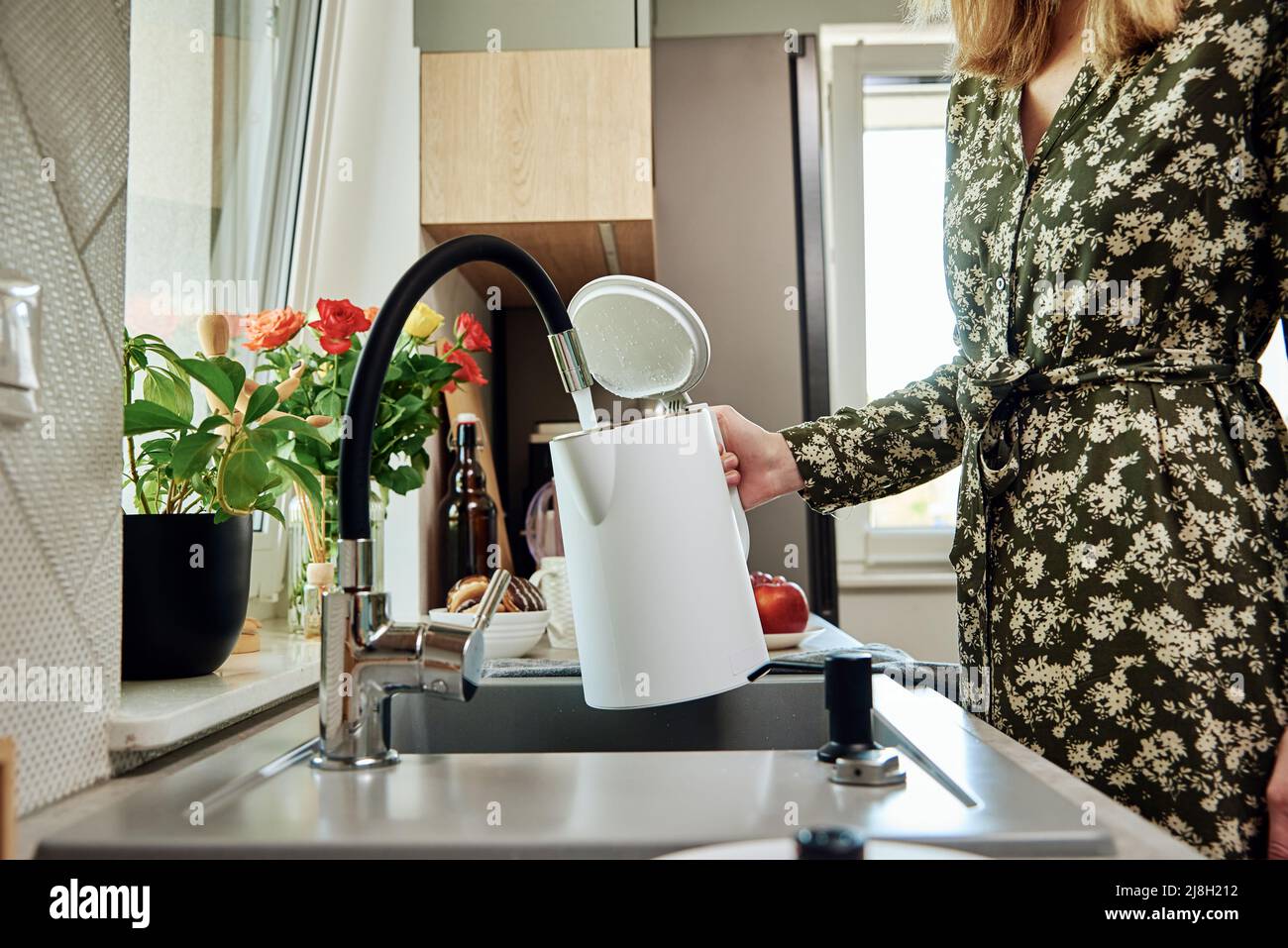 Woman pouring clean filtered water from faucet into electric kettle for boiling water at kitchen Stock Photo