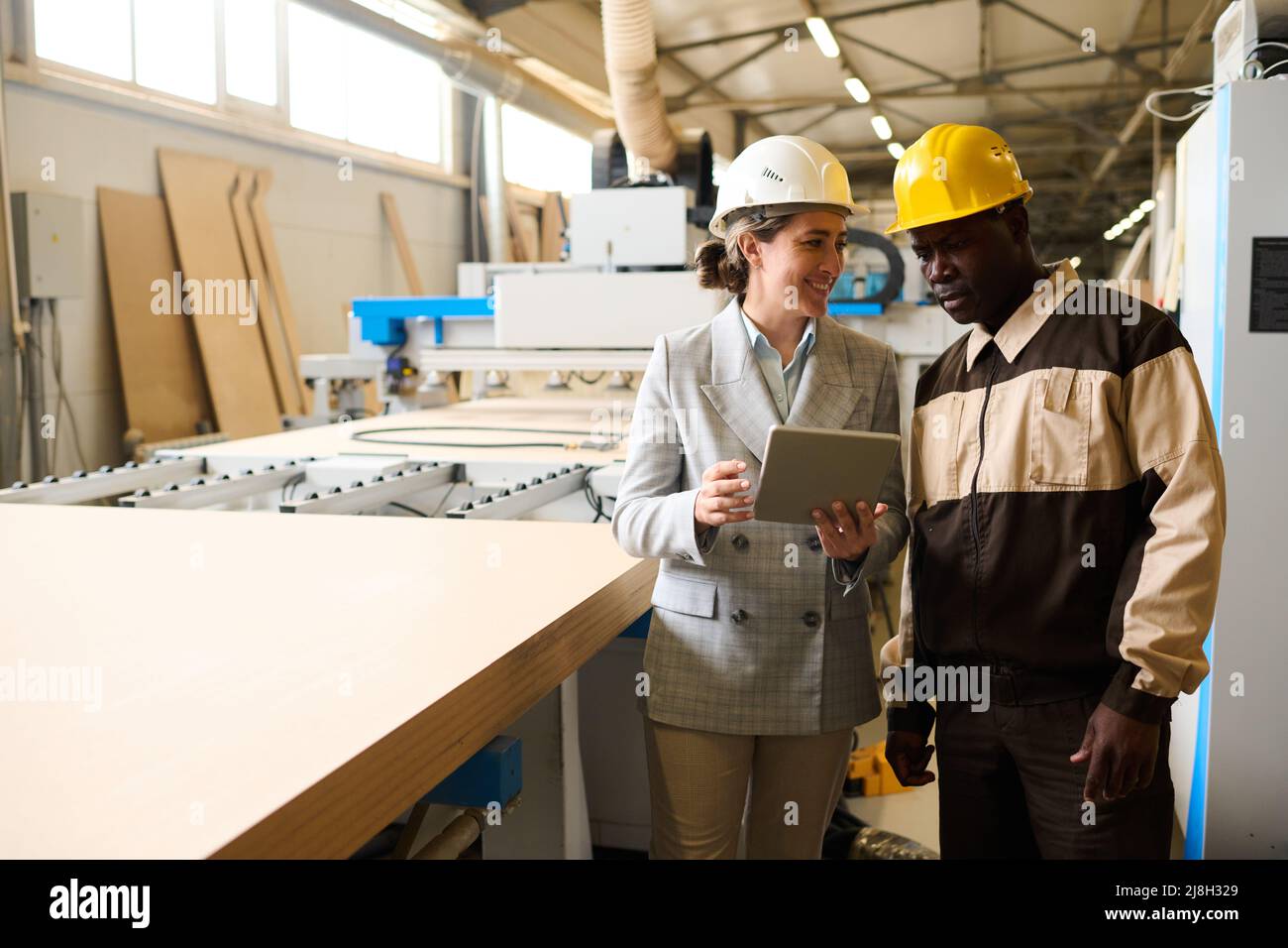 Engineer controlling the work at factory using tablet pc, she talking to foreman while they standing at machine Stock Photo