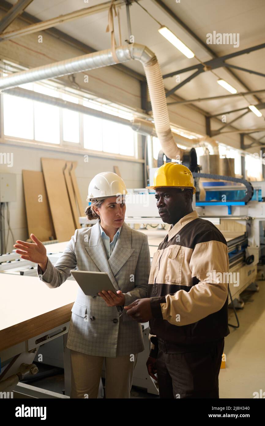 Young businesswoman using digital tablet and discussing working process with foreman at factory Stock Photo