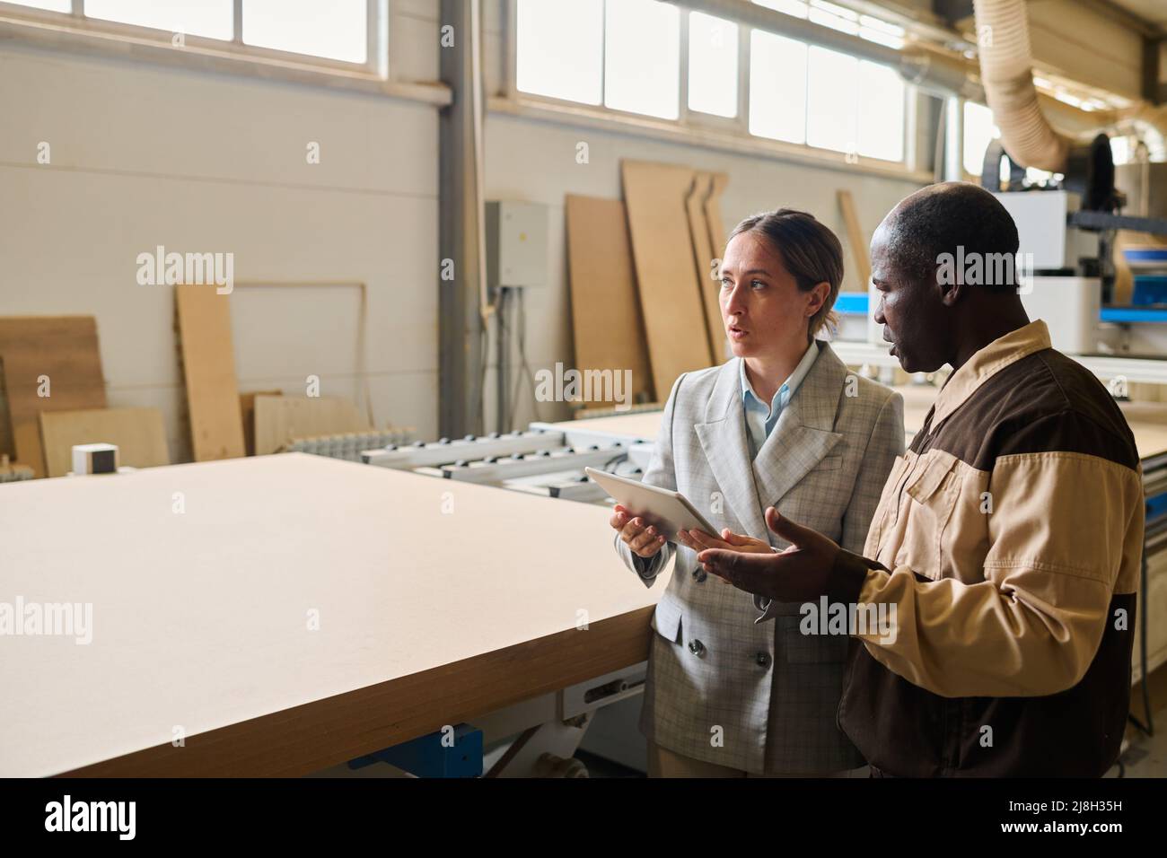 Female engineer using tablet pc and discussing work of machine with foreman at factory Stock Photo